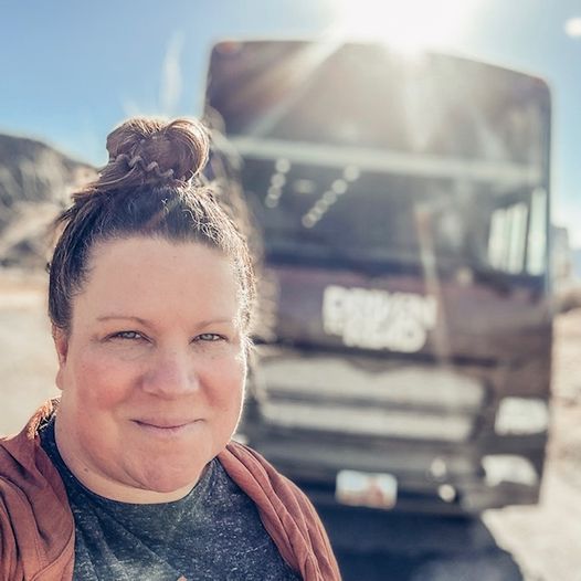 A smiling woman takes a selfie in front of a bookmobile as the sun shines down upon her 
