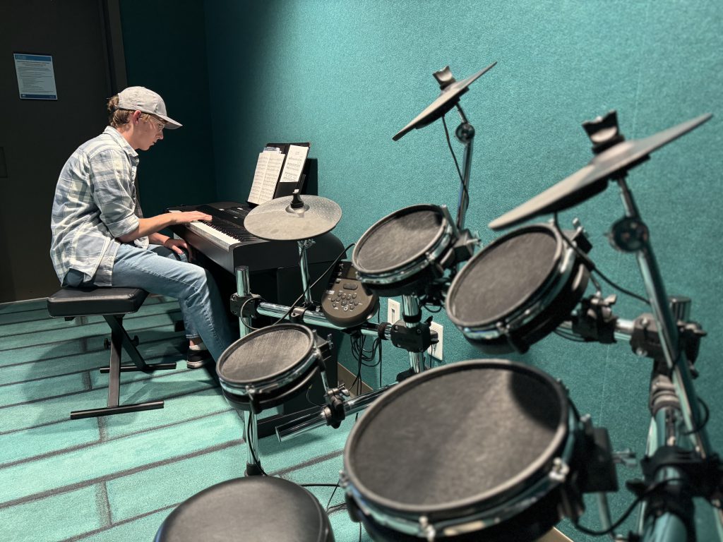 A young man uses the drums in the audio room of a library. 