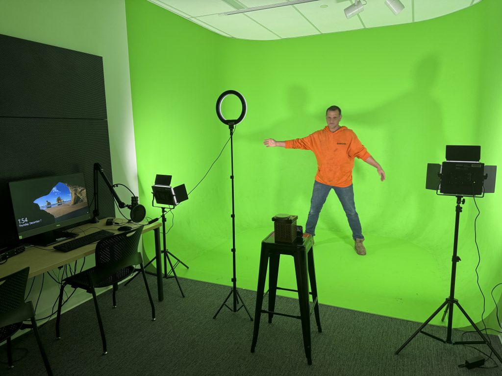 A young man uses a green screen in the Create Space inside of a library. 